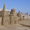 Castillo di sabbia dettagliato su una spiaggia affollata, con ombrelloni sullo sfondo.