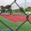 Persone giocano a tennis su campo recintato.