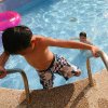Un bambino sale le scale fuori da una piscina, mentre un altro nuota vicino a un gonfiabile rosa.