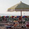 Spiaggia affollata con ombrelloni colorati e persone sdraiate sui lettini sotto il sole.