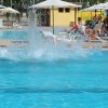 Una piscina con schizzi d'acqua e persone che si rilassano su lettini sotto ombrelloni.