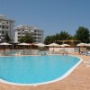 Una piscina con ombrelloni bianchi, lettini e edifici residenziali sullo sfondo.