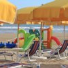 Ombrelloni e lettini gialli su una spiaggia con giochi colorati per bambini in lontananza.