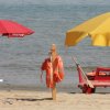 Spiaggia con ombrelloni gialli e rossi, una sedia a sdraio rossa e salvagenti.