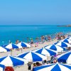 Spiaggia affollata con ombrelloni blu e bianchi, bagnanti in mare e sulla sabbia.
