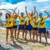 Gruppo di persone in magliette gialle allegre posa davanti al mare.