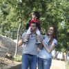 Una famiglia passeggia, con un bambino seduto sulle spalle di un adulto, in un parco alberato.