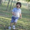 Bambino sorridente corre su un prato con alberi e luce del sole.