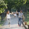 Tre persone camminano felici in un viale alberato, tenendo sollevato un bambino.