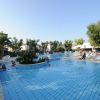 Piscina ampia con bambini, palme, e sdraio bianche.