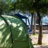 Una tenda verde in un campeggio tra gli alberi, con ombre sul telo.