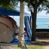 Una tenda sotto una tettoia blu vicino al mare, con una bicicletta appoggiata a un albero.