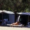 Una persona prende il sole su una sdraio vicino a tende da campeggio sotto gli alberi.
