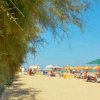 Spiaggia soleggiata con ombrelloni colorati e persone su lettini.