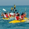 Persone in kayak gialli con giubbotti rossi pagaiando nel mare blu.