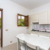 Una cucina con tavolo bianco, sedie e portafinestra aperta su un giardino.