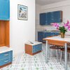 Cucina open space con mobili blu, tavolo da pranzo con fiori rosa e pavimento piastrellato.