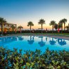 Piscina riflettente al tramonto con palme e strutture sullo sfondo.
