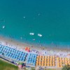 Spiaggia vista dall'alto, con ombrelloni blu e arancioni e mare azzurro.