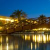 Ponte in legno illuminato sopra una piscina di notte, con palme sullo sfondo.