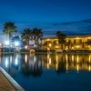 Piscina illuminata di notte con palme e un edificio sullo sfondo.