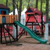 Area giochi con scivoli e casette colorate tra gli alberi.