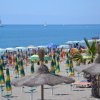 Spiaggia con ombrelloni colorati e barche a vela in mare.