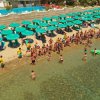 Spiaggia affollata con ombrelloni verdi, persone sulla sabbia e in acqua.
