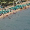 Spiaggia affollata con ombrelloni verdi e azzurri.