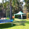 Area giochi con tappeto elastico, altalene e un gazebo su un prato verde.