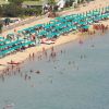 Spiaggia affollata con ombrelloni turchesi e bagnanti in mare.