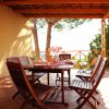 Terrazza con tavolo tondo in legno, sedie, piante e vista sugli alberi.