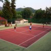 Persone giocano a tennis su un campo all'aperto circondato da alberi.