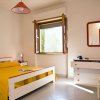 Una stanza con letto matrimoniale giallo, finestra aperta e comò bianco con specchio.