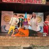 Bambini in costume su un palco con un adulto sdraiato davanti.