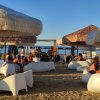 Persone sedute sotto ombrelloni in spiaggia al tramonto.