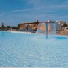 Una piscina con una fontana centrale, circondata da sedie a sdraio e un cielo azzurro.