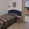 Camera con letto, copriletto a righe blu e marroni, terrazza con tavolo e sedie arancioni.
