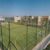 Campo sportivo verde circondato da una recinzione, vicino a edifici gialli e al mare.