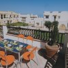 Terrazza con tavolo apparecchiato e sedie arancioni, vista su edifici bianchi.