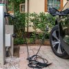 Auto elettrica in carica presso una stazione di ricarica, con verde sullo sfondo.