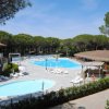 Area piscina con due vasche, ombrelloni bianchi, lettini e un edificio con tetto di paglia.