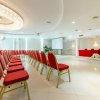 Sala conferenze con sedie rosse, podio e schermo proiettore.