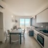 Interno moderno con cucina, tavolo, sedie e vista sul mare da una porta-finestra.