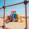 Un colorato parco giochi sulla sabbia, visto attraverso una rete di corda.