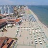 Ampia spiaggia con file di ombrelloni bianchi e verdi, edifici alti sul lungomare.