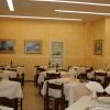 Ristorante con tavoli apparecchiati, tovaglie bianche, pareti giallo chiaro e quadri.
