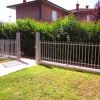 Giardino verde con siepi e recinzione metallica.