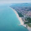 Città costiera con lunga spiaggia sabbiosa e mare blu, vista dall'alto.