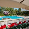 Piscina all'aperto con sedie a sdraio rosse, ombrelloni e alberi sullo sfondo.